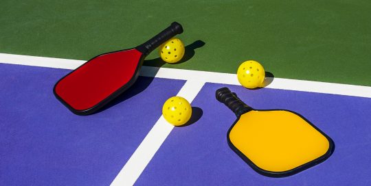 pickleball-set-of-two-paddles-and-two-balls-laid-out-on-a-pickleball-court (1)