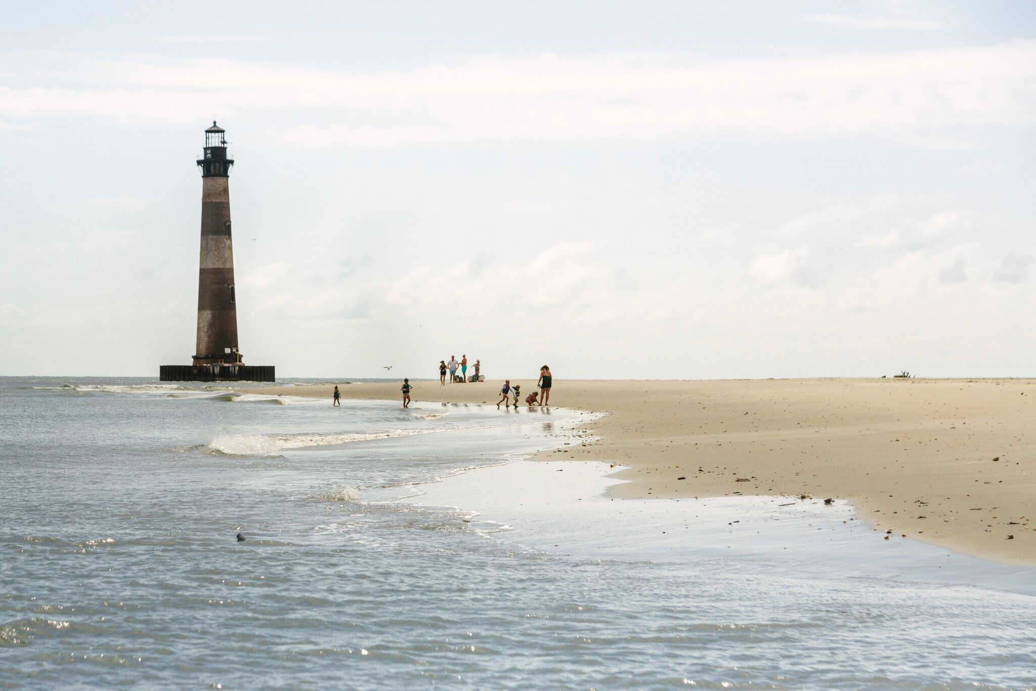 A lighthouse located on a beach with the shore coming in and a blue sky with some clouds.