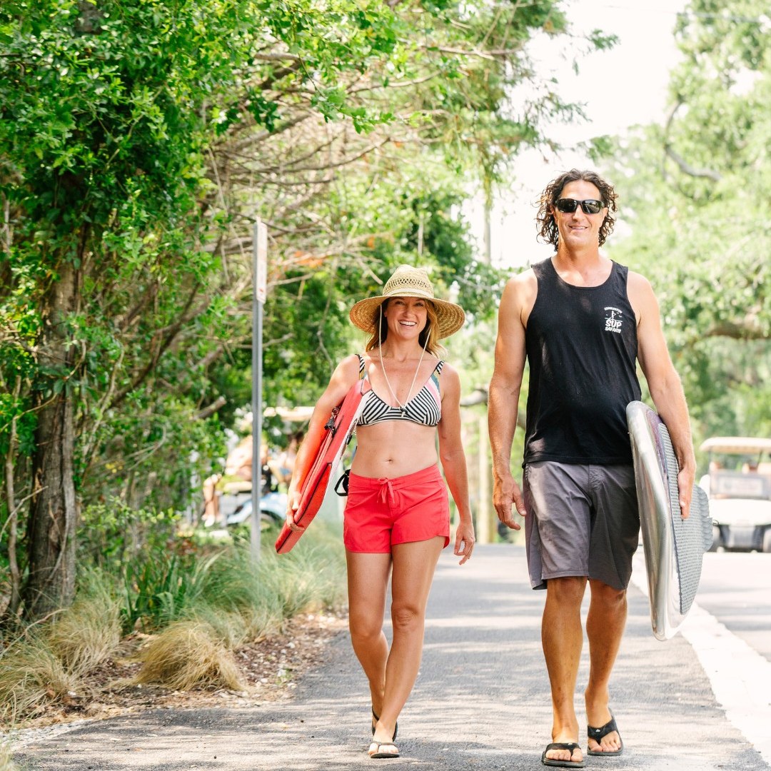617555441_1288299716659466_4252732780175360382_n couple walking along the road with surfboards